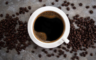 Black coffee in a white glass placed on an old cement table with coffee beans.